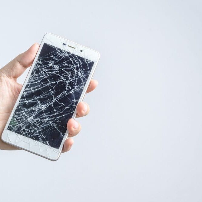 Hand holding mobile phone with broken screen A person holding an iphone with broken screen.