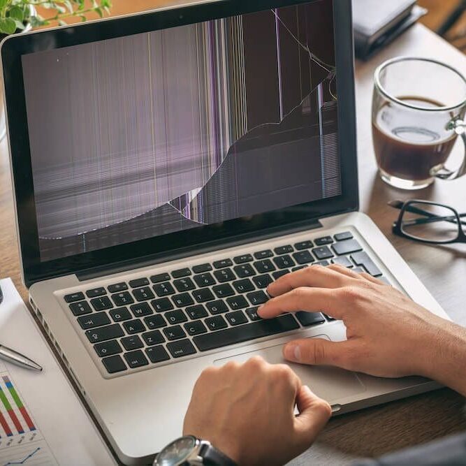 Laptop Screen Repair Services: 5 Essential Qualities to Consider. Trust California Computer for Expert Solutions. broken laptop screen on an apple while man is working